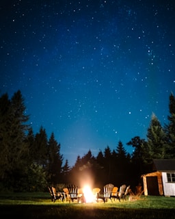 A cozy campfire setup with chairs and a starry night sky in the background.