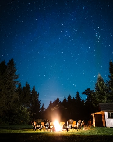 A cozy campfire setup with chairs and a starry night sky in the background.