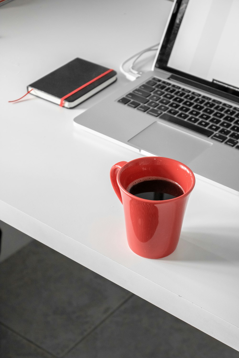 흰색 나무 책상 위에 맥북 프로 옆에 커피가 담긴 빨간 세라믹 머그잔