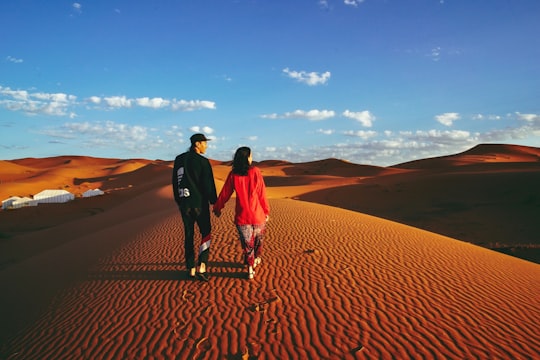man and woman walking on vast desert during daytime in Erg Chebbi Morocco