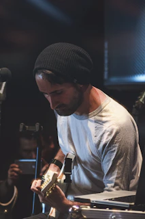 A student practicing guitar while following a live interactive music lesson on a laptop.