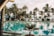 A tranquil resort setting with a large, inviting swimming pool surrounded by palm trees. In the background, lounge chairs and umbrellas are neatly arranged, creating a relaxing atmosphere. The reflection of the palm trees in the water enhances the serene ambiance.