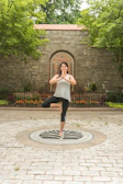 A smiling woman practicing yoga outdoors at sunrise, surrounded by trees.