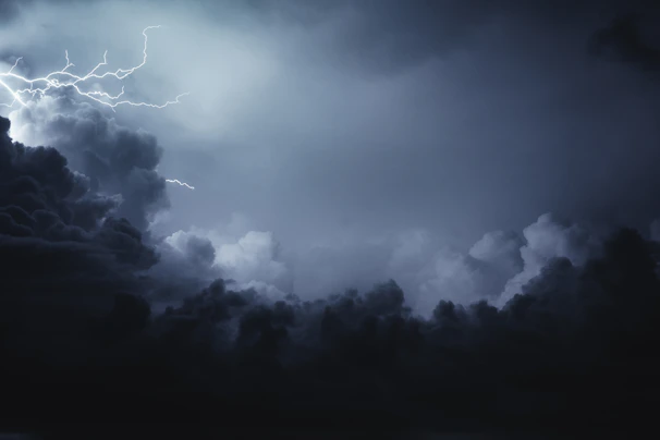 A dramatic stormy sky with dark thunderclouds and a flash of lightning in the distance.