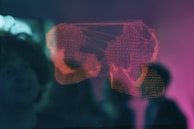 A digital wireframe of boxing gloves illuminated in red appears against a blurred, dark background. The design seems to be part of a 3D display or hologram, projecting a modern and futuristic aesthetic. Nearby, there is an indistinct silhouette of a person observing the display.