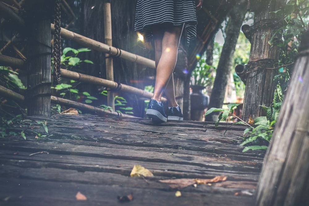 woman wearing black sneakers walking on wooden pathway