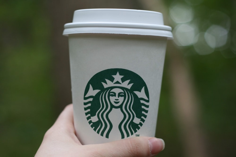 person holding green and white disposable Starbucks tumbler