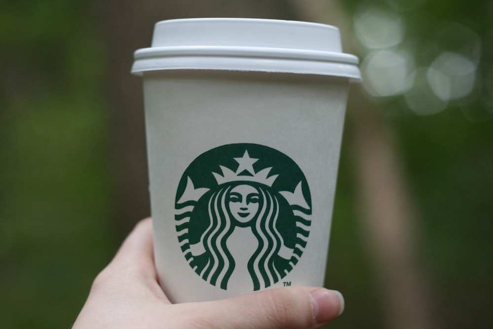 persona sosteniendo un vaso desechable verde y blanco de Starbucks