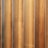 Vertical wooden planks with a natural finish are aligned in a parallel pattern. The wood has visible grain and variation in shades, creating a textured appearance. The planks are evenly spaced and have a warm, earthy tone.