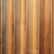 Vertical wooden planks with a natural finish are aligned in a parallel pattern. The wood has visible grain and variation in shades, creating a textured appearance. The planks are evenly spaced and have a warm, earthy tone.
