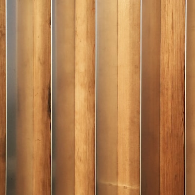 Vertical wooden planks with a natural finish are aligned in a parallel pattern. The wood has visible grain and variation in shades, creating a textured appearance. The planks are evenly spaced and have a warm, earthy tone.