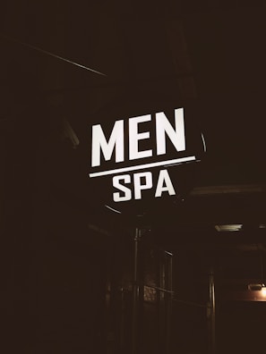 A brightly illuminated sign featuring the words 'MEN SPA' is displayed in a dark, industrial-looking environment. The sign stands out in contrast to the dim surroundings, providing a focus point against the otherwise shadowy backdrop.
