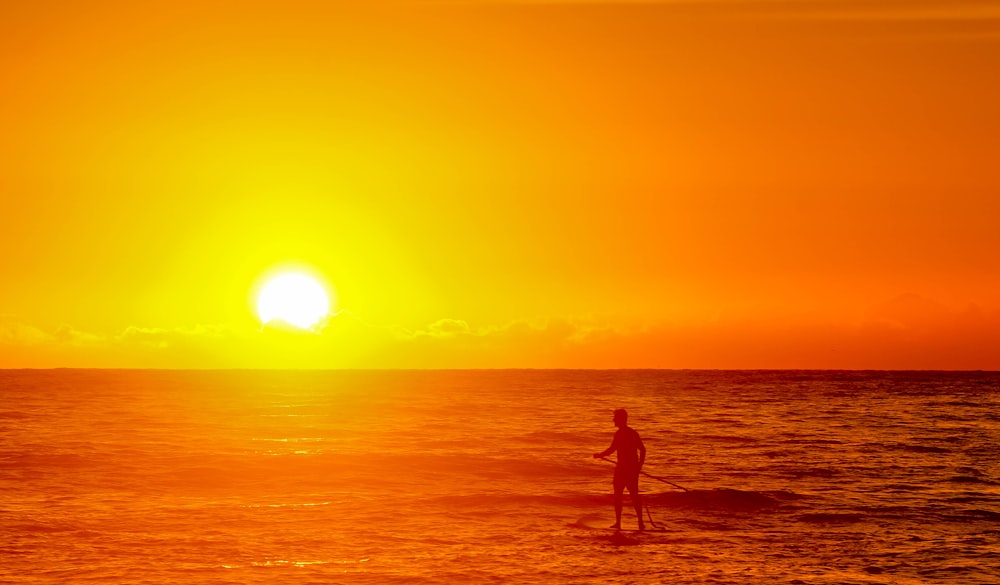 silhouette photo of person on body of water during golden hour