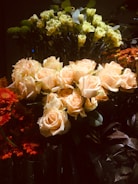 A lush arrangement of various flowers including creamy white roses, bright green carnations, and vibrant orange gerberas. The dark background accentuates the vivid colors of the blooms, creating a striking contrast.