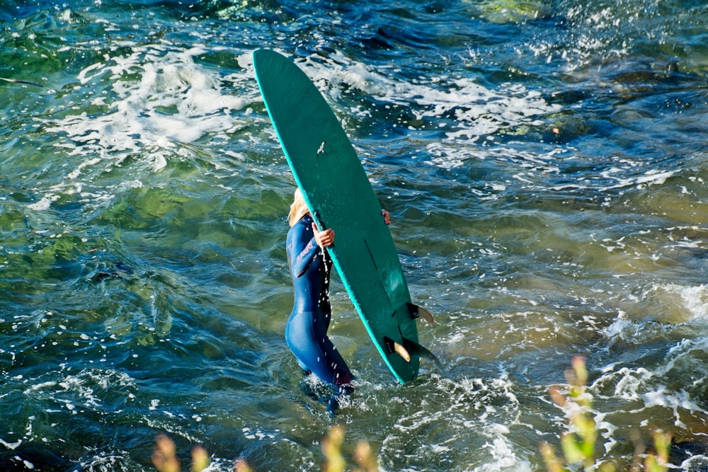 Persona parada en el agua cargando una tabla de surf