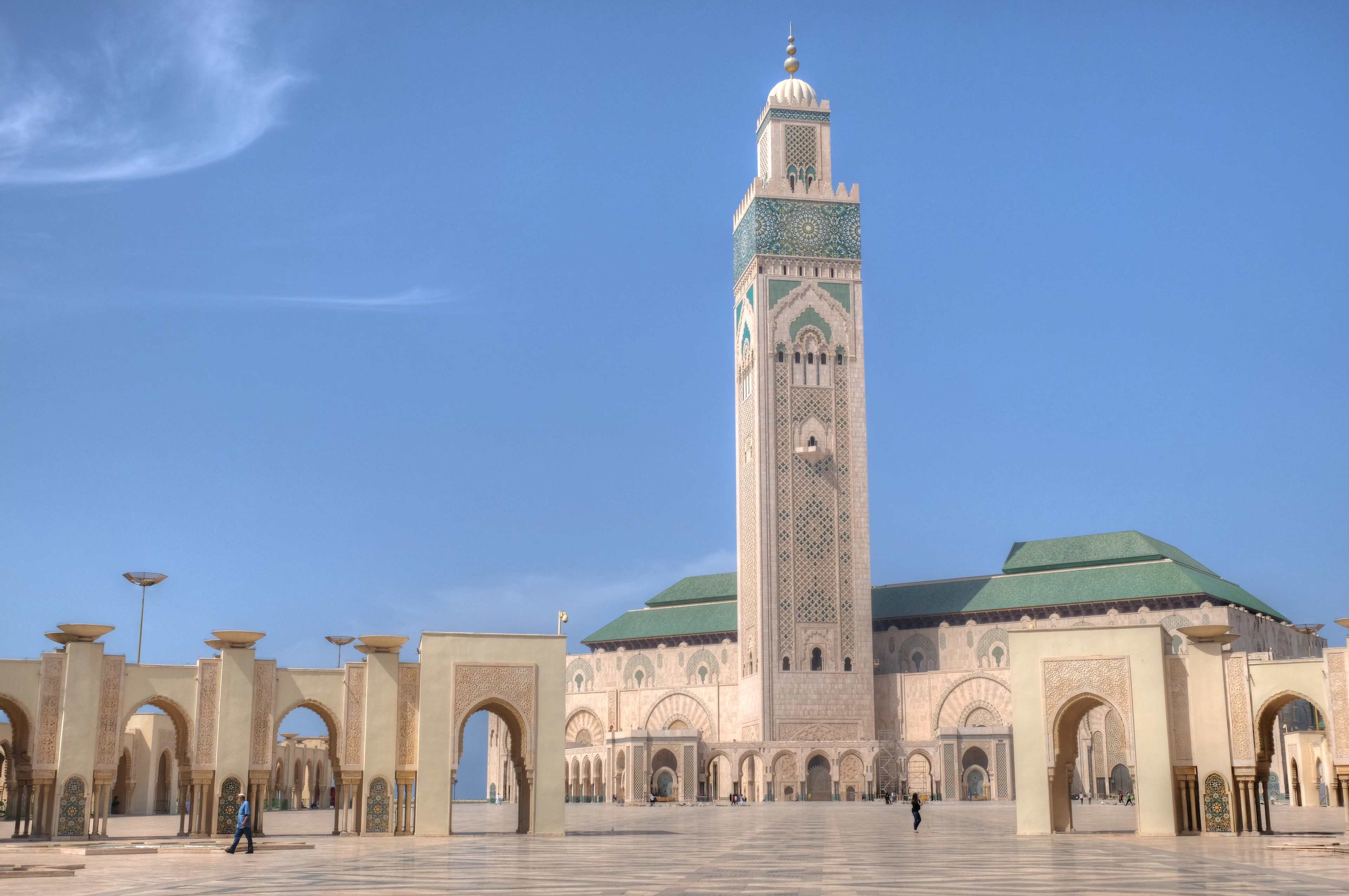 The Hassan II Mosque in Casablanca with its towering minaret and green-tiled roofs above a marble esplanade under a blue sky
