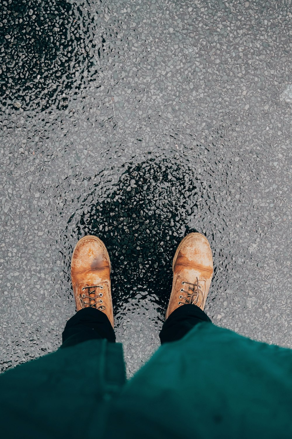 photo of person wearing pair of brown leather lace-up boots standing on black concrete ground