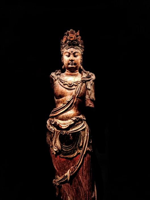 A beautifully carved wooden statue standing tall against a neutral background, showcasing fine craftsmanship.