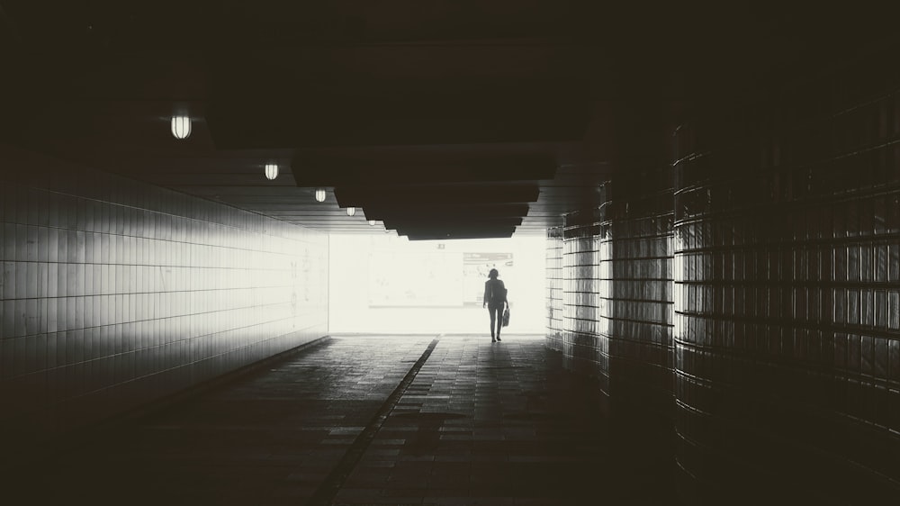 gray scale photography of person walking in bridge