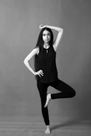 Yoga practitioner holding a graceful pose in soft beige bodysuit against a clean white background.