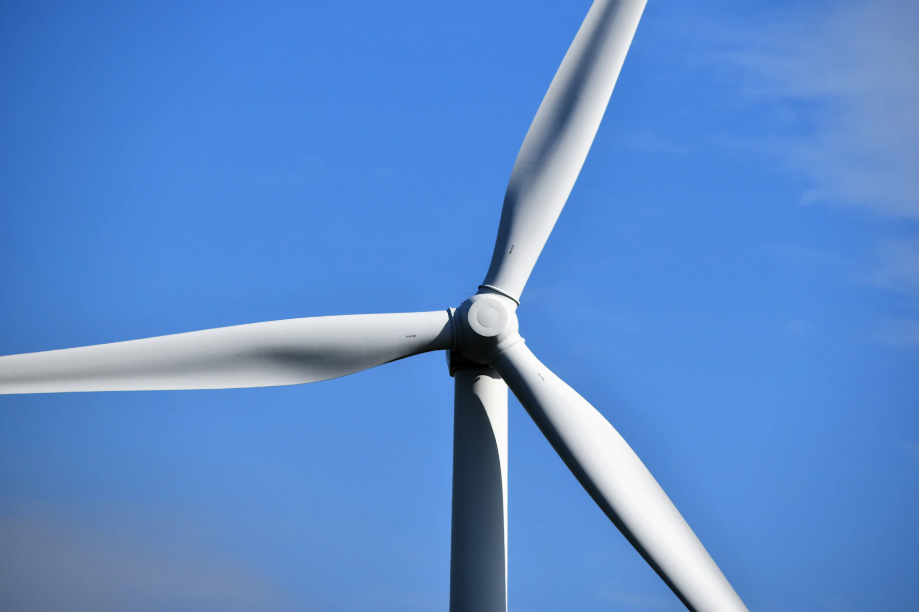 A white turbine blade and hub seen from directly below against blue sky