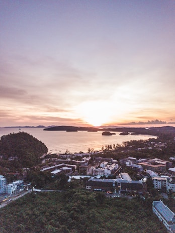 A wide aerial view of a coastal village at sunset, colors melting into the sea and horizon.
