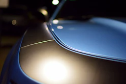 Close-up of a luxury car's glossy black hood reflecting the sky during a professional mobile detailing session.