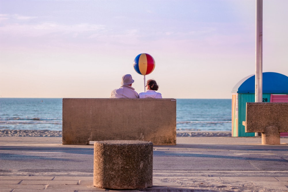 two person sitting on bench near sea during daytime