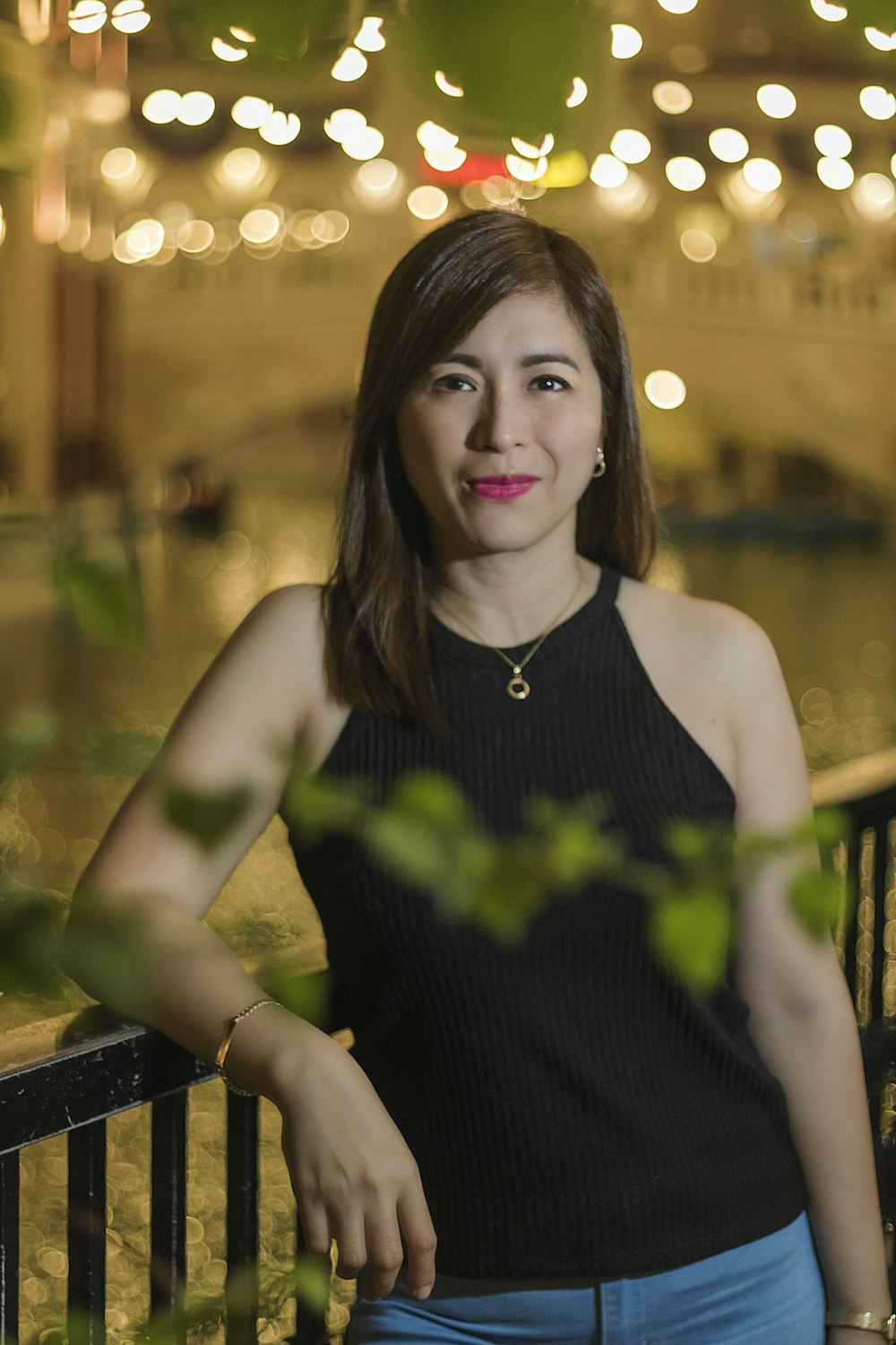 smiling woman wearing black spaghetti strap top standing and leaning near railings