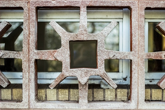The image captures part of a wall with decorative concrete blocks featuring geometric patterns. Each block has a star-like shape with protruding points surrounding a central square opening. Behind the concrete structure, there are windows, partially covered.