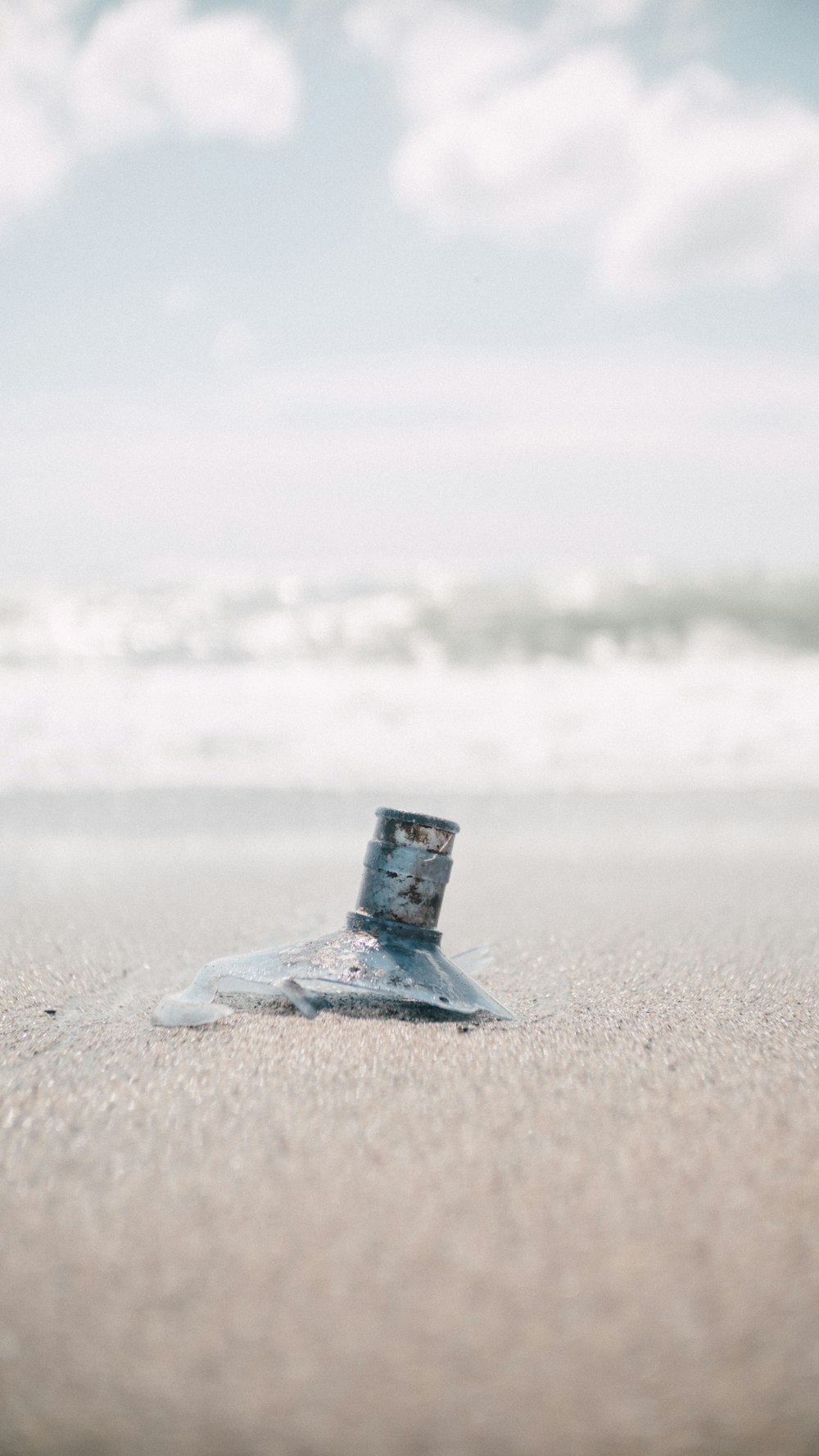 a broken glass bottle sitting on top of a sandy beach