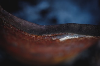 A close-up view of a rusted metal surface with a smooth, curved edge. The texture shows signs of corrosion, and the background is blurred with a gradient of dark blue tones.