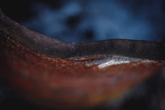 A close-up view of a rusted metal surface with a smooth, curved edge. The texture shows signs of corrosion, and the background is blurred with a gradient of dark blue tones.