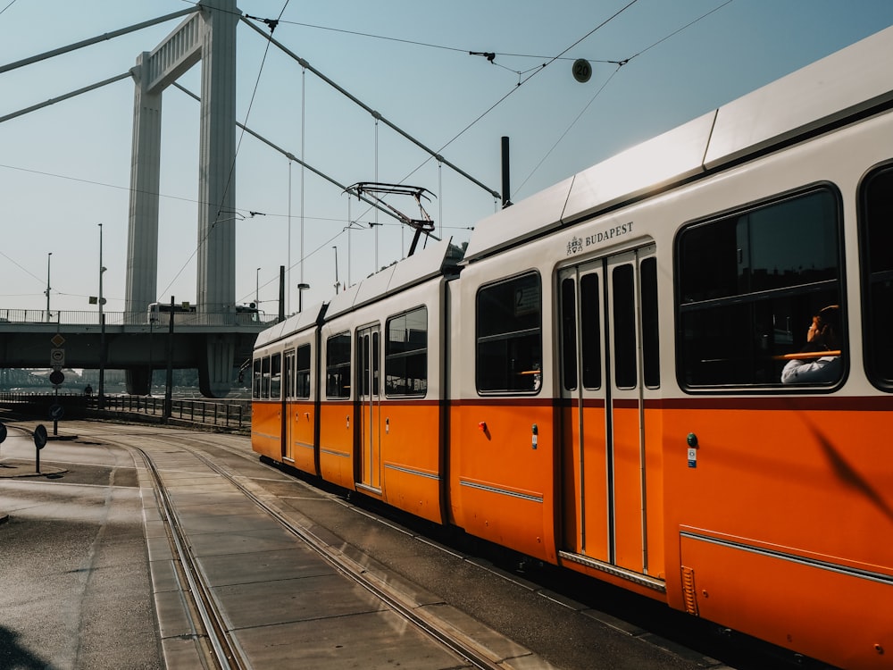 white and orange train near suspension bridge