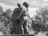 A sculpture depicting an embrace between two figures, likely a parent and child. The figures are captured in a moment of deep connection and emotion, with delicate details in their clothing and posture. Trees and sky form the natural background, adding to the serene atmosphere.