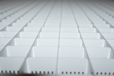 A close-up view of a grid-like arrangement of white plastic squares, creating a repetitive geometric pattern. The squares appear to be part of a larger structure, possibly a partition or organizer.