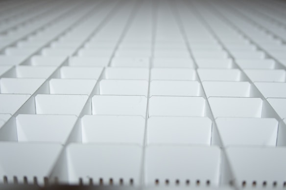 A close-up view of a grid-like arrangement of white plastic squares, creating a repetitive geometric pattern. The squares appear to be part of a larger structure, possibly a partition or organizer.