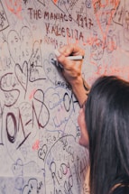 A person signing a canvas with colorful art supplies around.