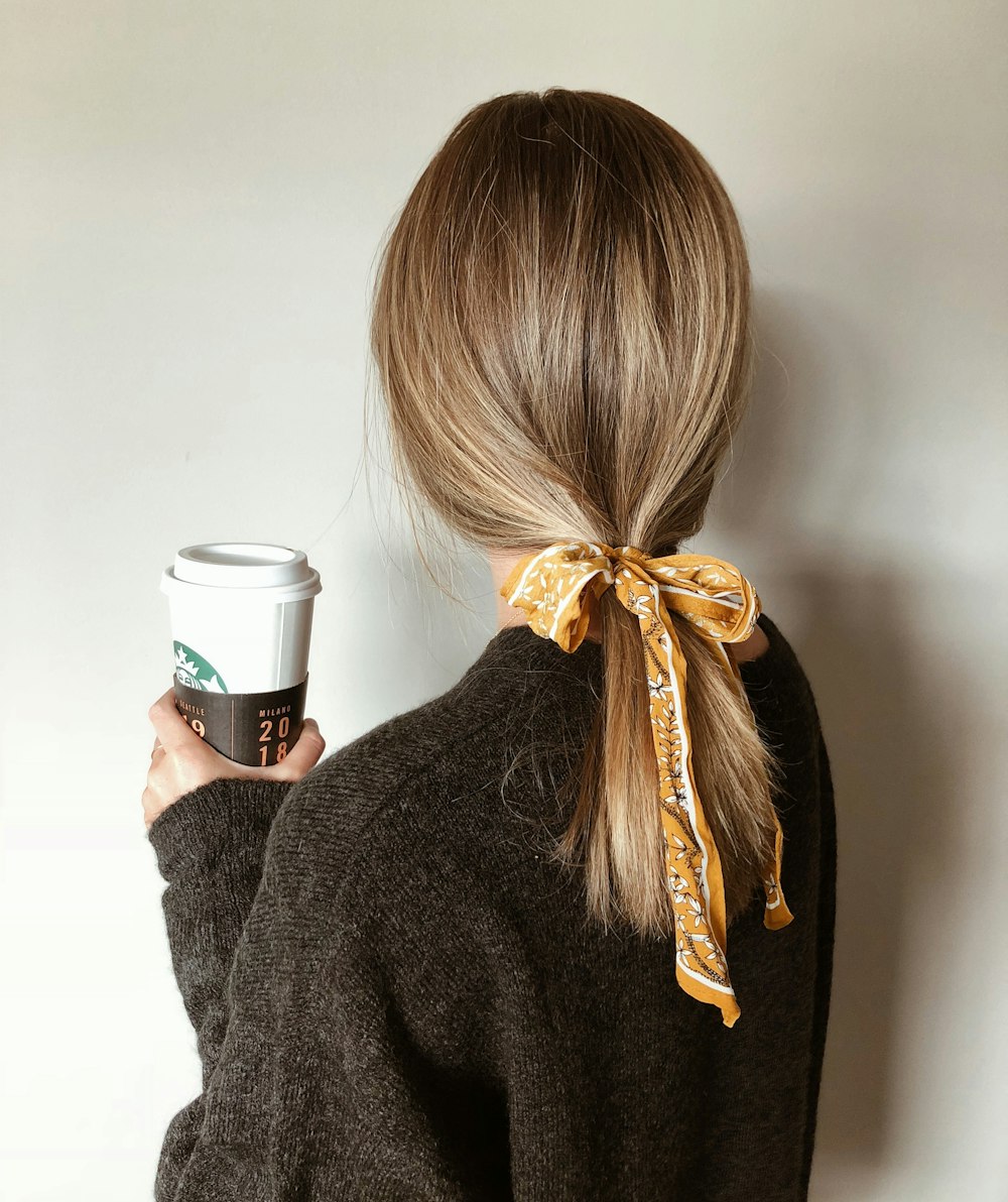 Mujer en suéter negro sosteniendo taza de café Starbucks