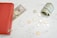 A red wallet with a golden zipper rests on a marble surface with a partially visible fifty-dollar bill sticking out. Nearby, a roll of one-dollar bills and loose change, including quarters and pennies, are scattered around.