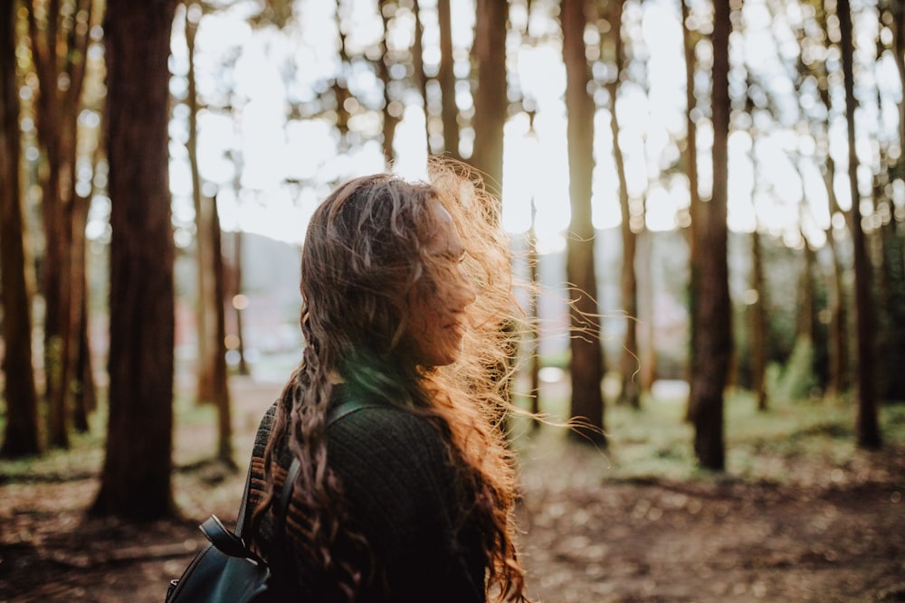 woman standing in middle of trees looking right