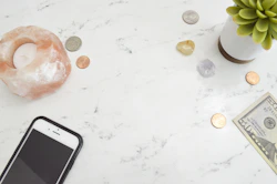 cell phone, spare change, a candle & a fifty dollar bill on a table, representing the cost to start 