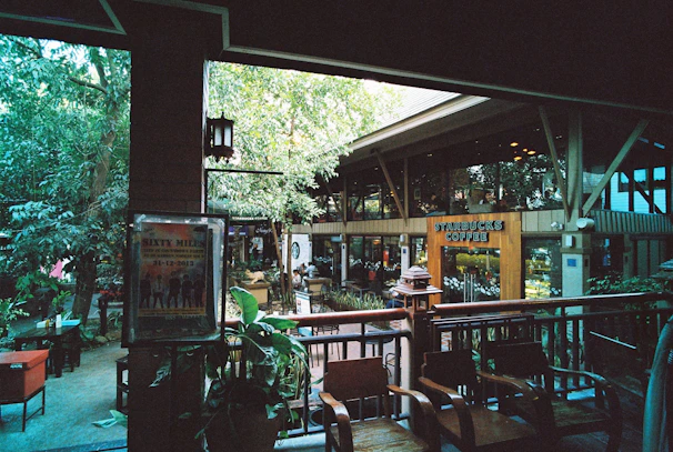 Cozy coffee shop patio with seating and lush greenery around.