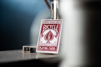 A deck of Bicycle brand playing cards with heritage design series, automobile No. 2 back, is placed in focus, with a blurred background. The card deck, mostly white with red design elements, is captured on what appears to be a tabletop.