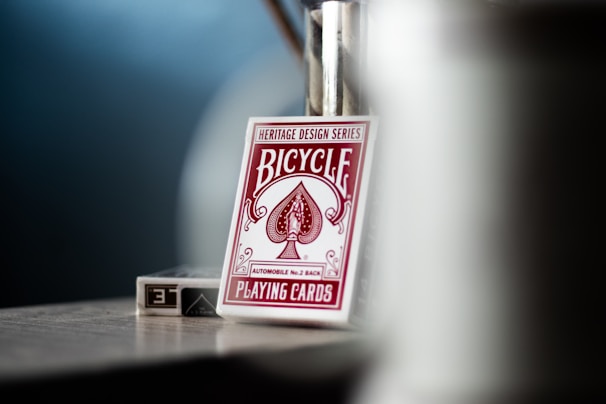 A deck of Bicycle brand playing cards with heritage design series, automobile No. 2 back, is placed in focus, with a blurred background. The card deck, mostly white with red design elements, is captured on what appears to be a tabletop.