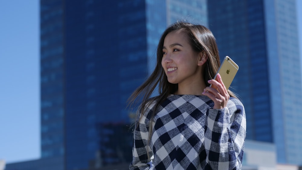 高層ビルの近くで金色のiPhone 6を手にする女性
