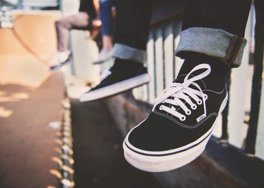 person sitting on rail wearing black Vans sneakers