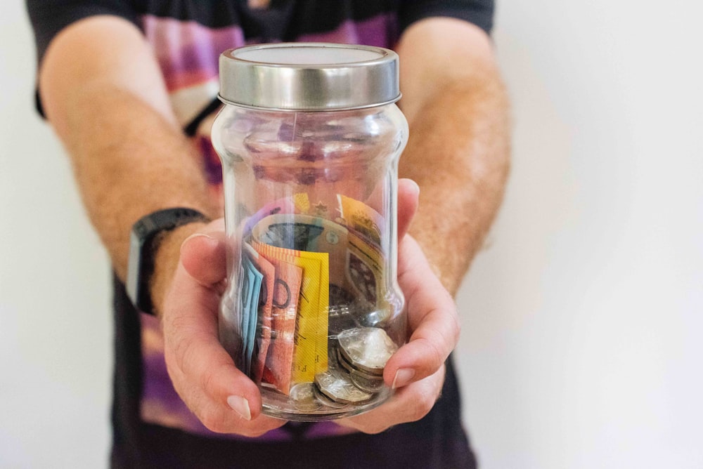 Un étudiant freelance avec un pot contenant de l'argent, des billets et des pièces.