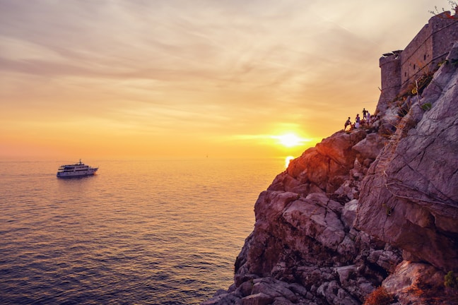 A vibrant boat sailing near the rocky coastline of Arraial at sunset.