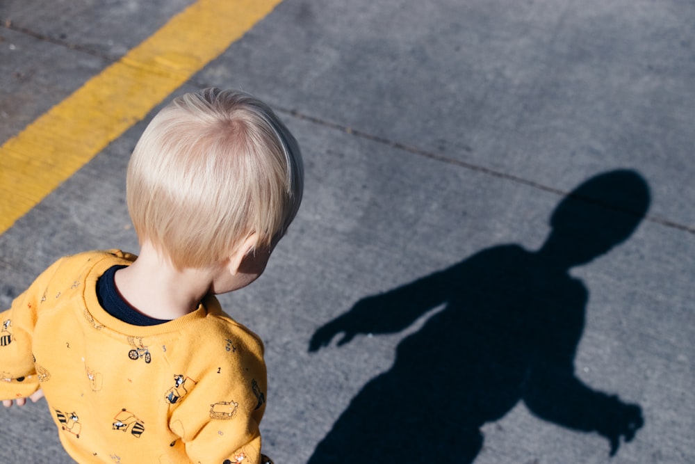 Junge steht auf der Fahrbahn und schaut tagsüber auf seinen Schatten